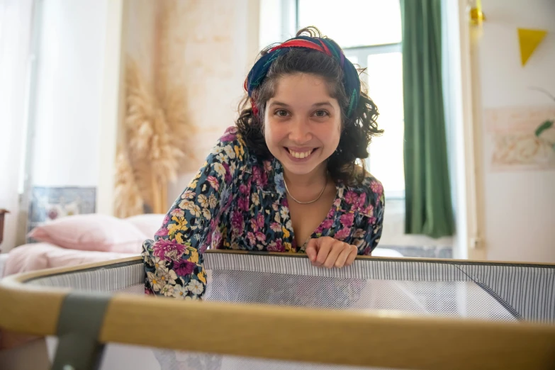 a woman smiling at the camera while looking behind her crib