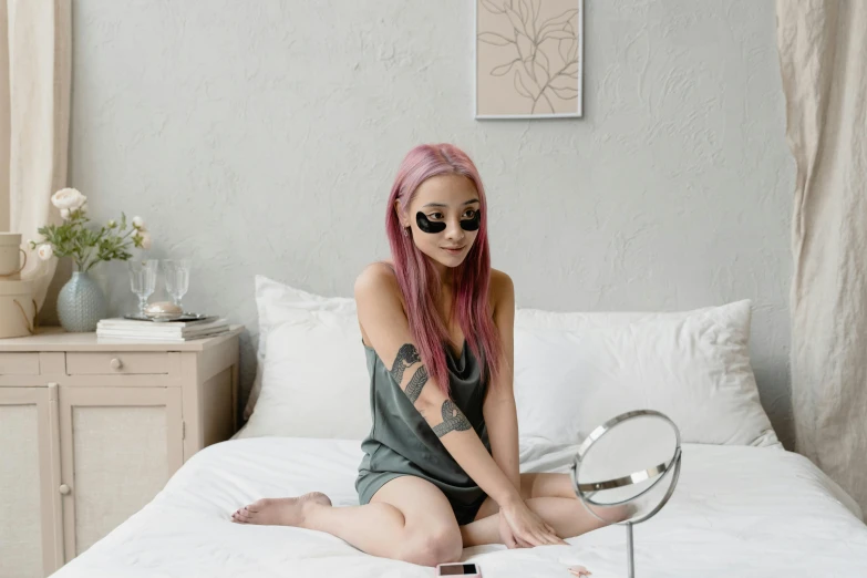 woman with bright pink hair sitting on a bed looking at the mirror