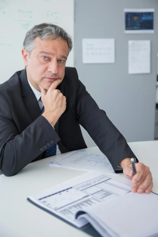 a man with gray hair wearing a business suit sitting at a white table