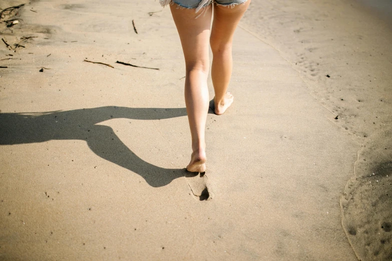 the back of a girl wearing flip flops and shorts walking on the beach