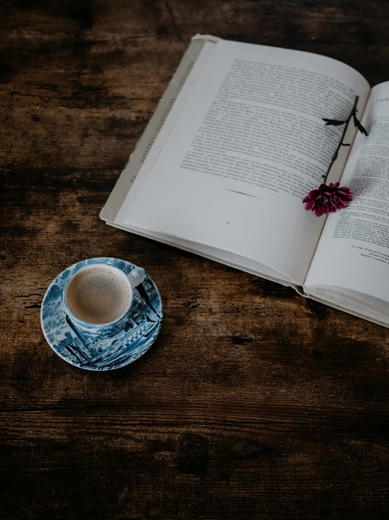 a cup of tea with an open book and a flower