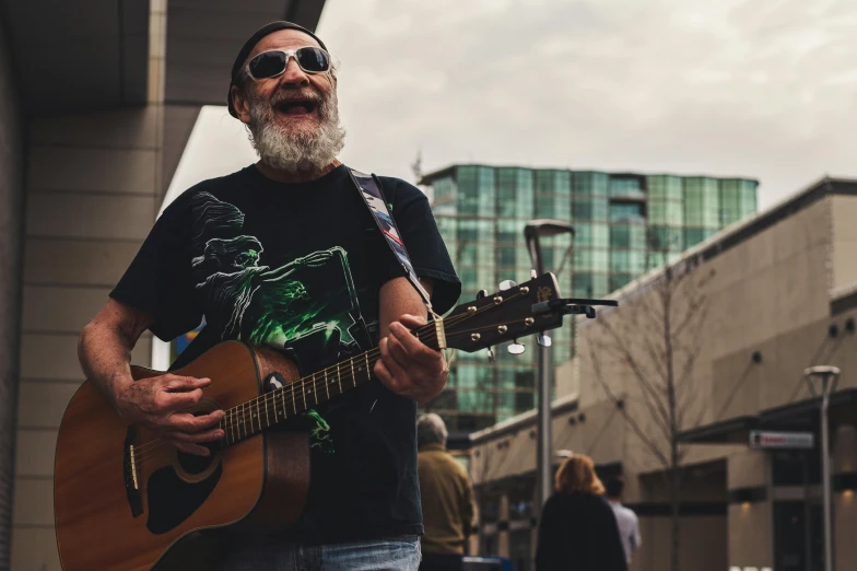 an older man with sunglasses playing guitar on the sidewalk