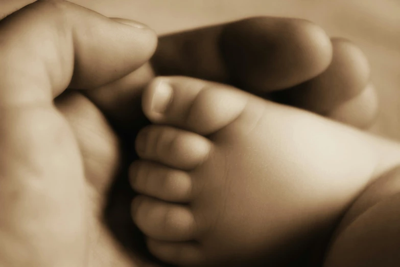 a person holding the baby's toes of another persons hand