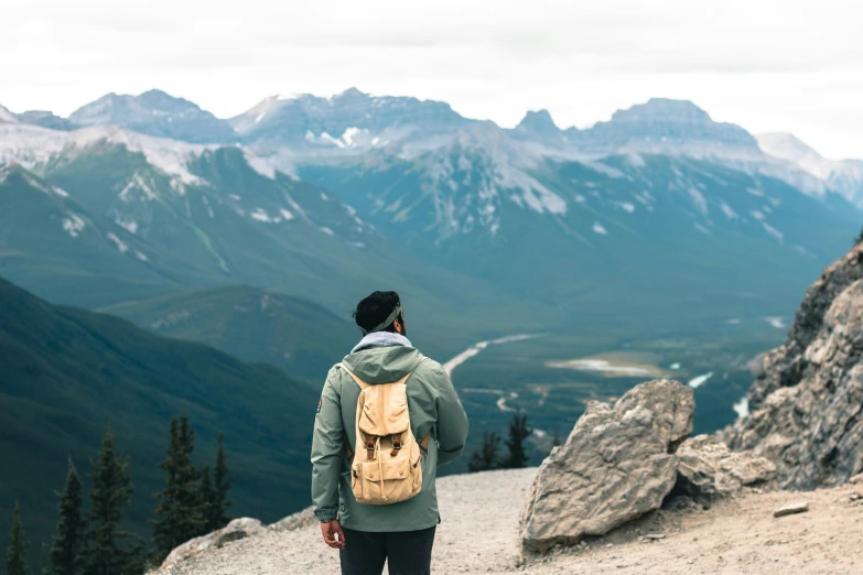 a man in a jacket standing on a hill above a mountain