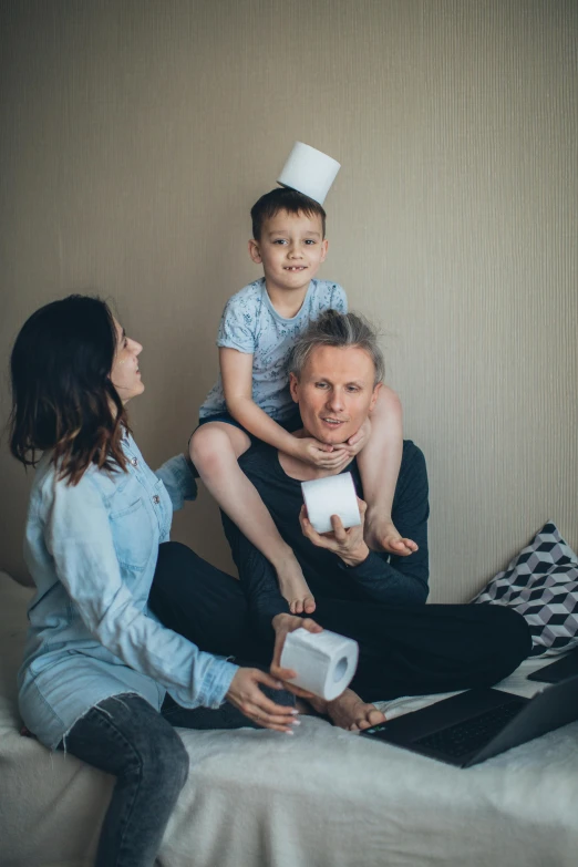 a woman is sitting on a bed while a small boy is holding an older man