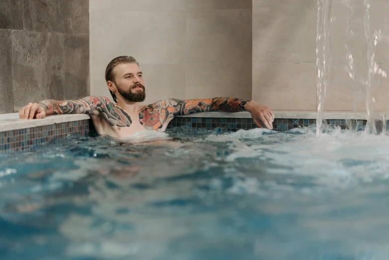 a tattooed man is sitting in the jacuzzi of a pool