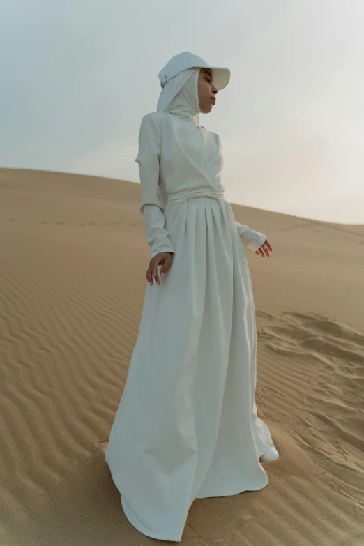 a woman in white and a white hat stands in sand dunes