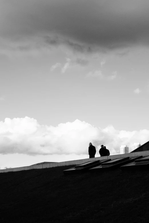 a couple of people standing on top of a hillside under a cloudy sky