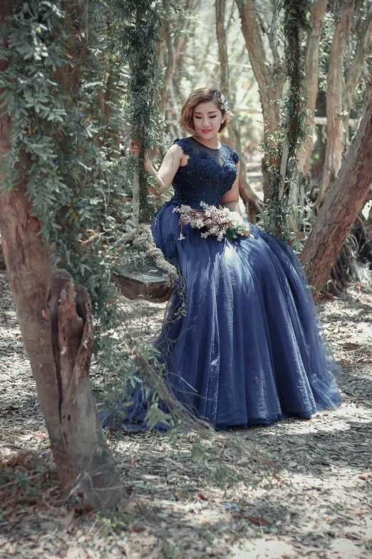 a young woman in a blue dress sitting in a tree grove