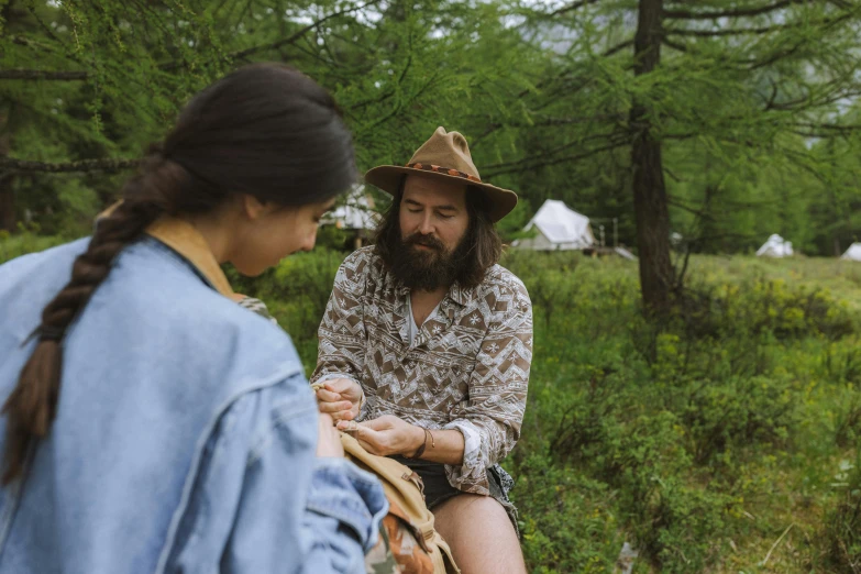 there is a man with long hair sitting on a bench talking to a woman