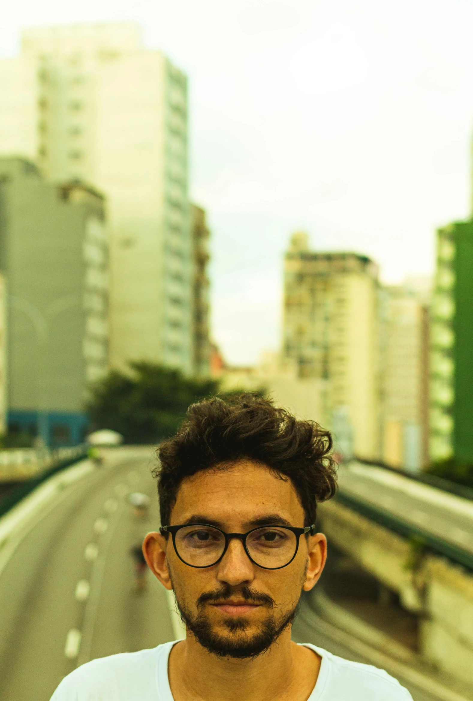 a young man wearing glasses stands on a bridge