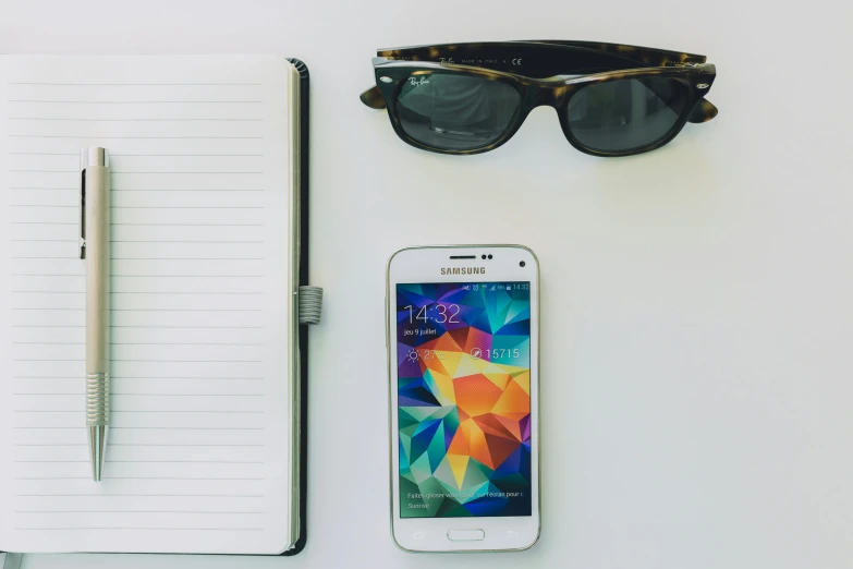 glasses, pen, notebook and cell phone sitting on a table