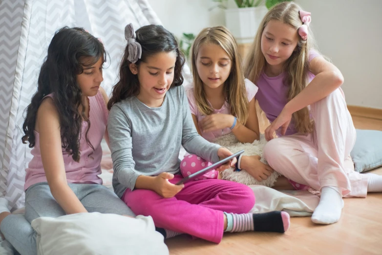 four little girls sit on the floor playing with a tablet