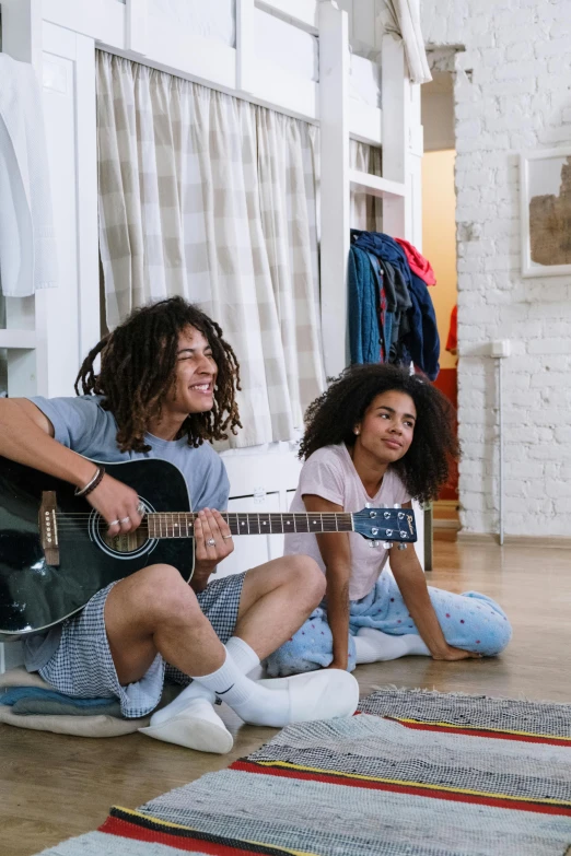 two girls are sitting on the floor playing guitars