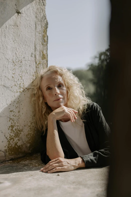 a beautiful blond woman leaning against a stone wall