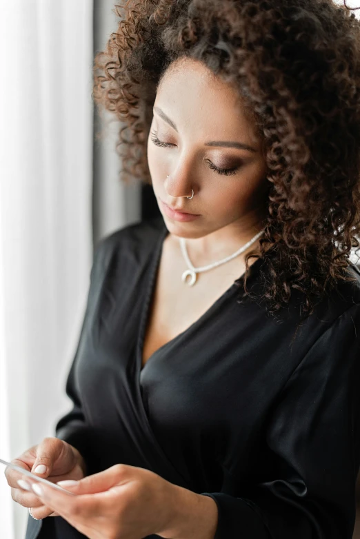 a young woman checks her cell phone in front of a window