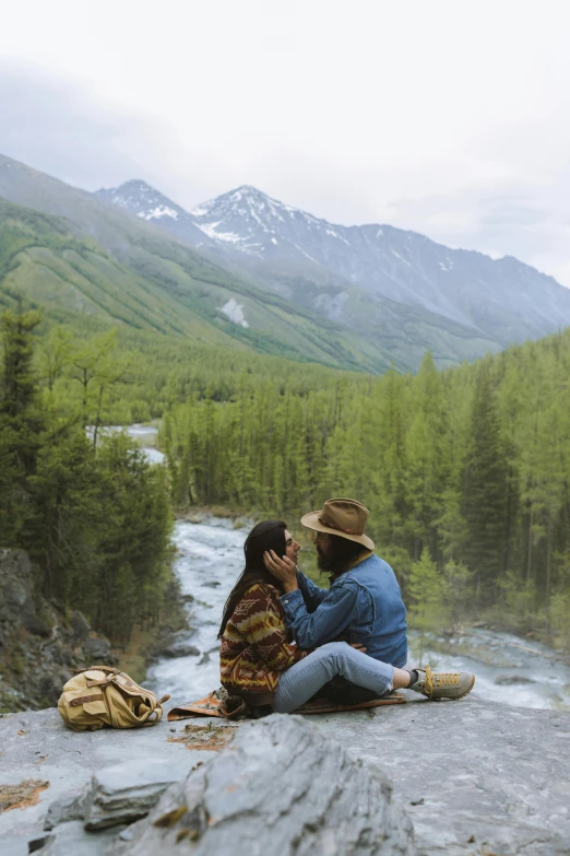 a couple is sitting on the edge of a cliff by a stream