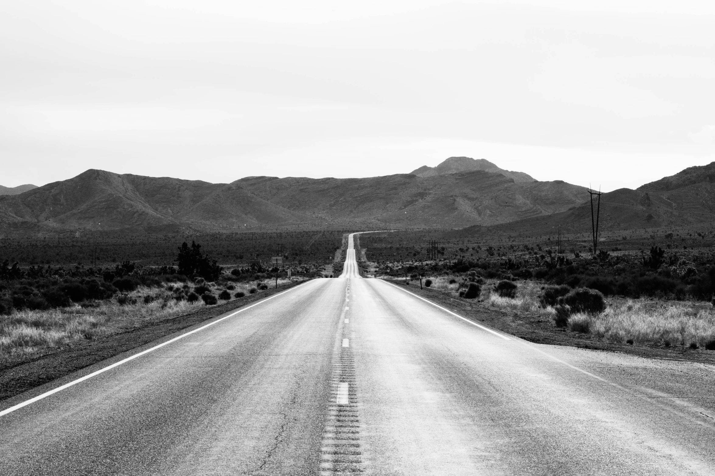 black and white image of an empty highway near mountains