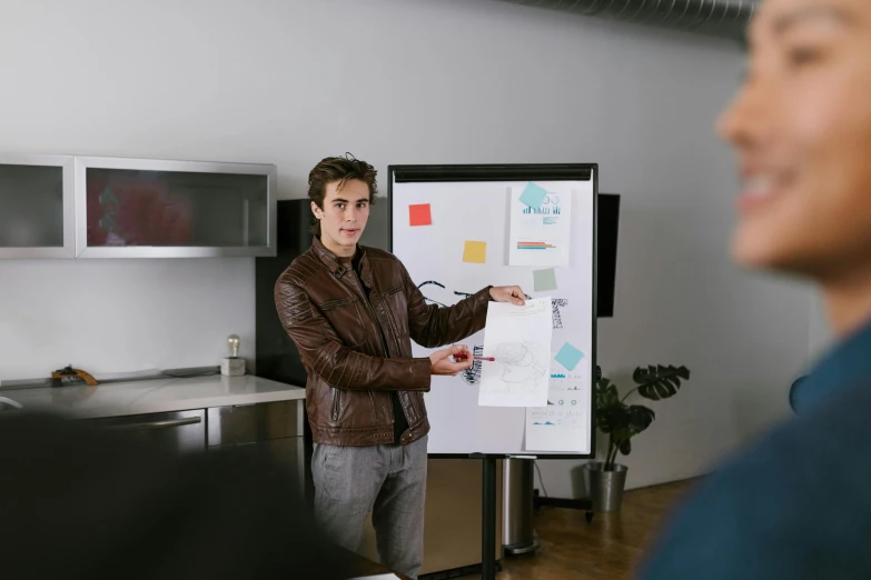 a man pointing to a whiteboard with different color labels