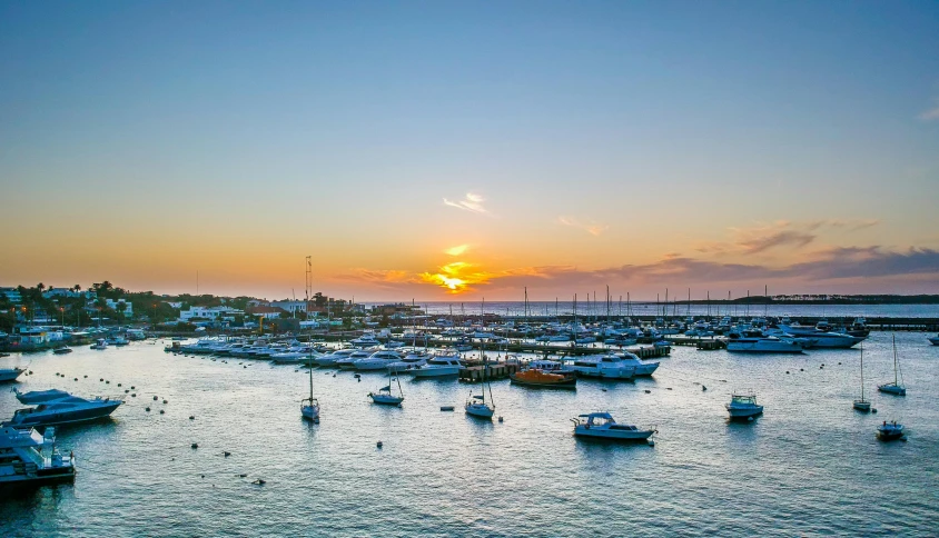 a boat harbor is filled with sailboats and the sun setting