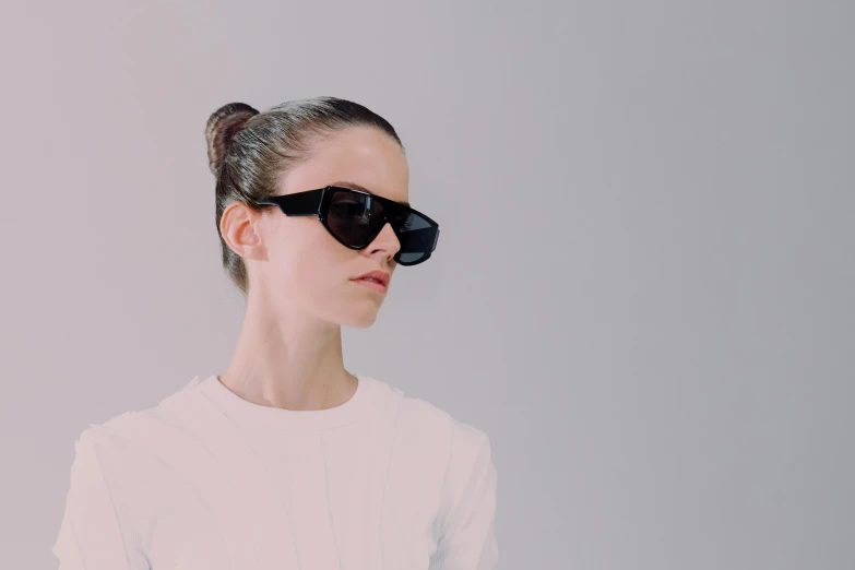 a woman wearing sunglasses while standing next to a white wall