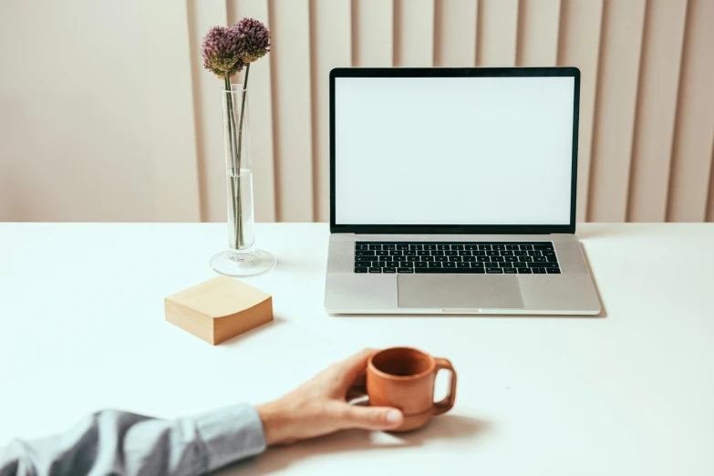 someone holds their hands near a mug and laptop