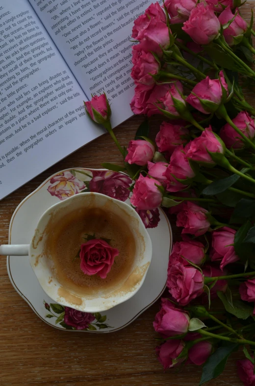 an open book and a cup on a saucer with rose petal