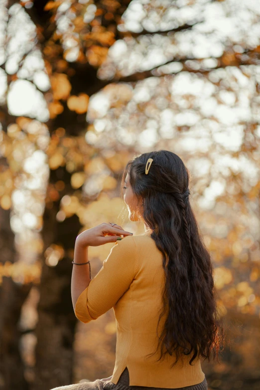 a woman sitting on a bench next to a tree in an autumn setting