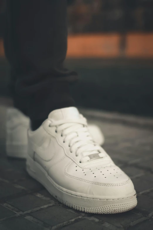 a person standing on a bricked floor next to white sneakers
