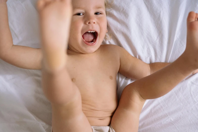 a baby laughing in his diaper on a bed