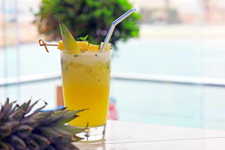 a glass of pineapple juice next to an individual sitting on a table