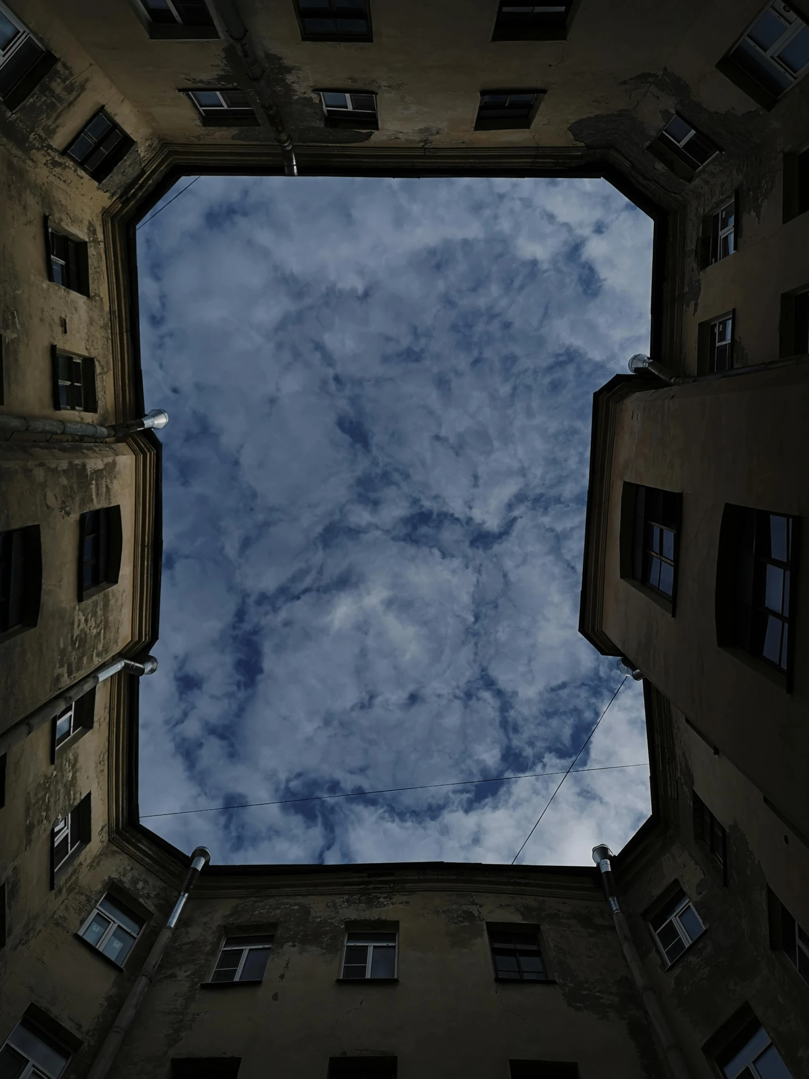 the view looking up from between buildings to a cloudy sky