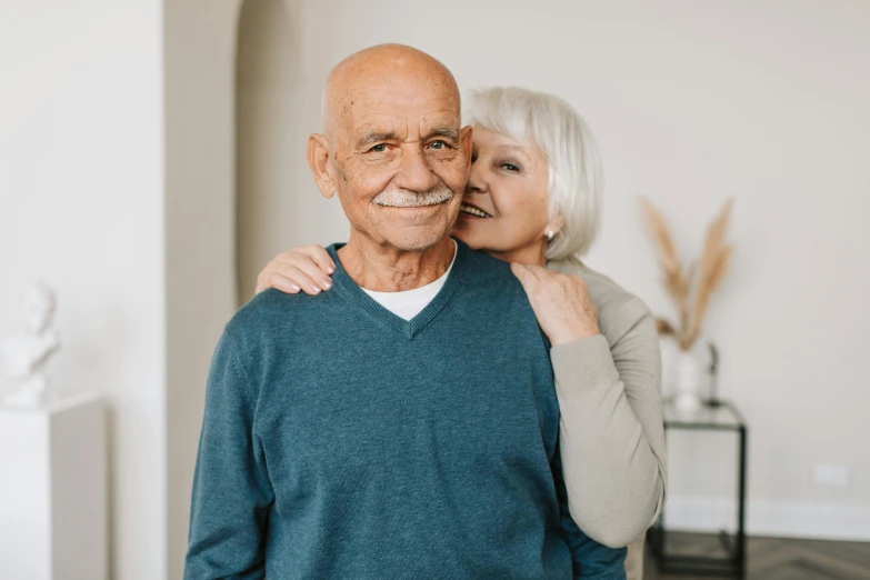 an old man and woman hug as they pose in their living room