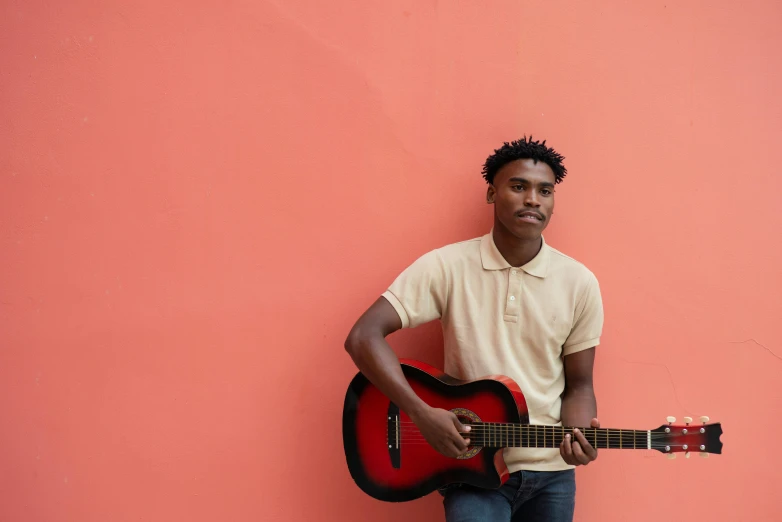 a man leaning against a pink wall holding a guitar