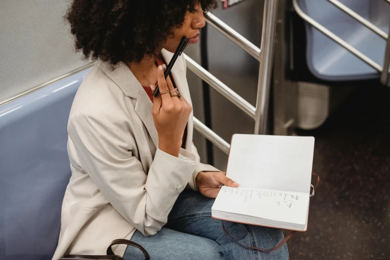 the woman is sitting on a train holding her notebook and taking a break