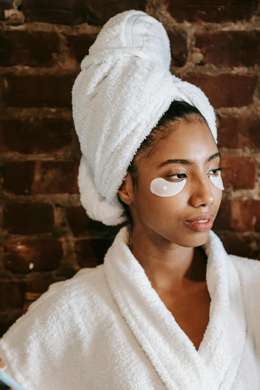 a woman in towel holding an eye patch with eye patches on her face