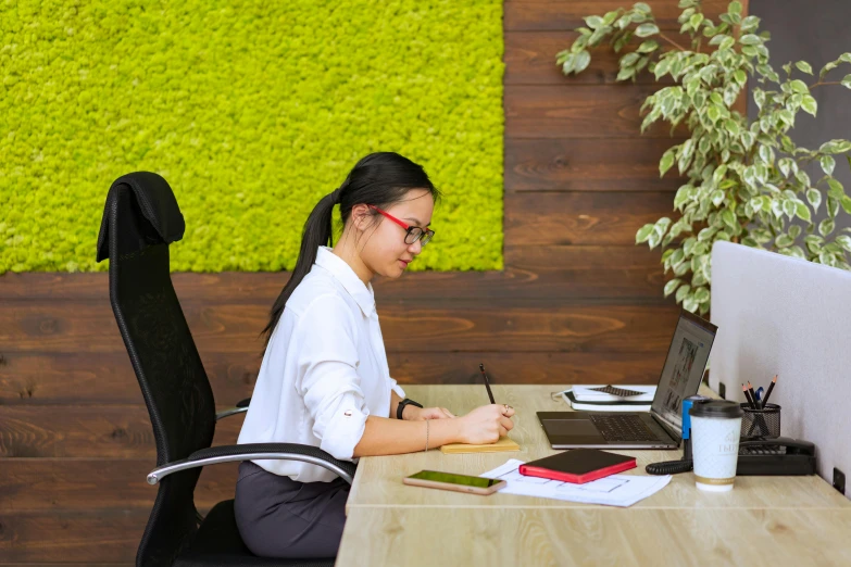 a woman sits at a desk writing on her laptop