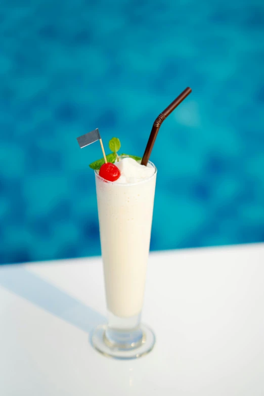 a cocktail garnished with cherry and ice in front of a swimming pool