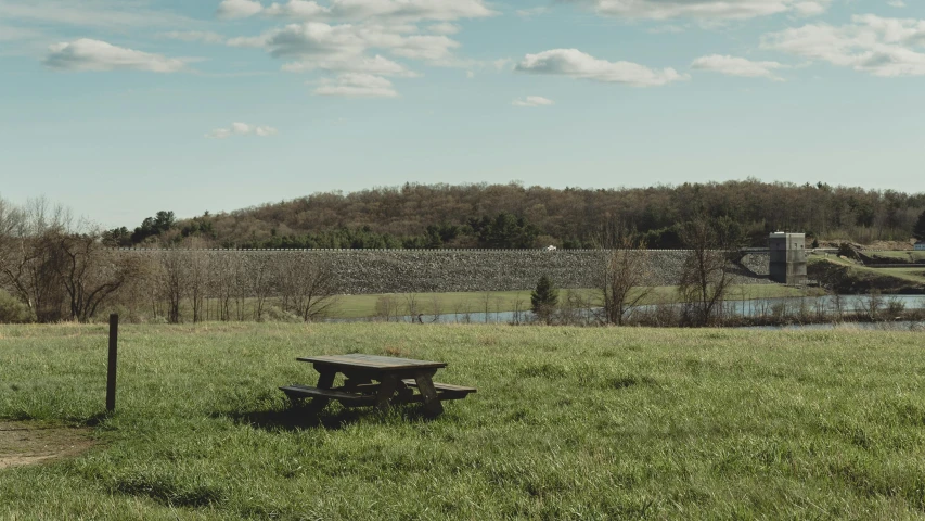 an empty picnic table in a field with a wall and trees in the background