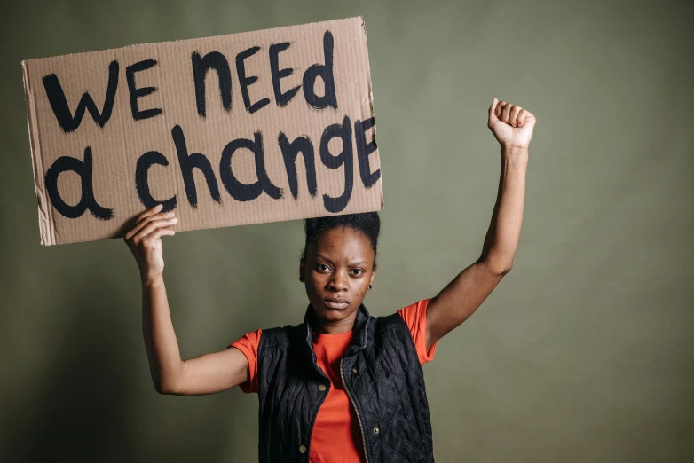 a woman holding a cardboard sign that reads we need a change