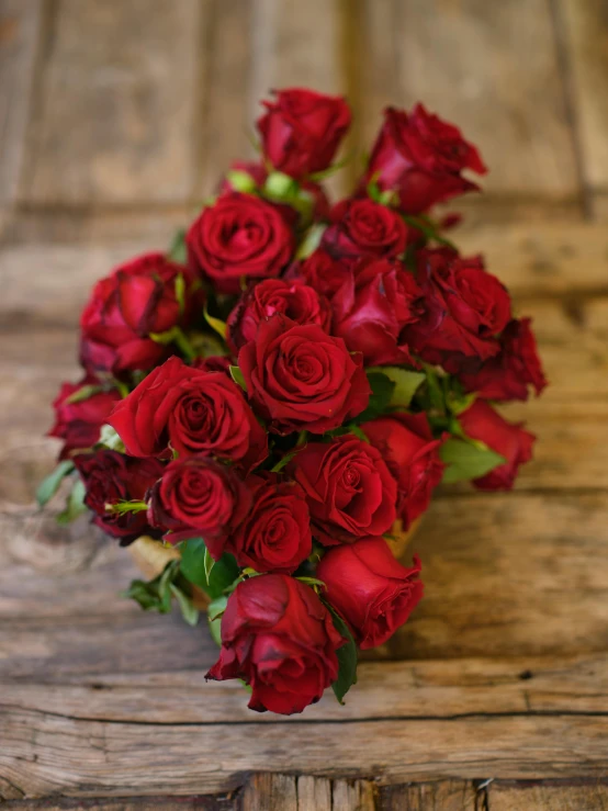 the bridal bouquet of roses is wrapped with twine of red ribbon