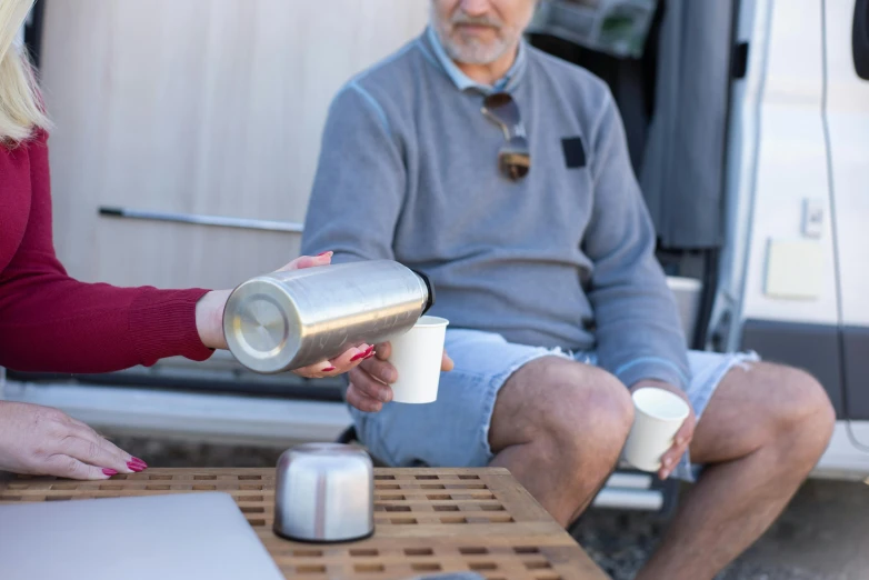 two people are outside sitting down and holding coffee mugs