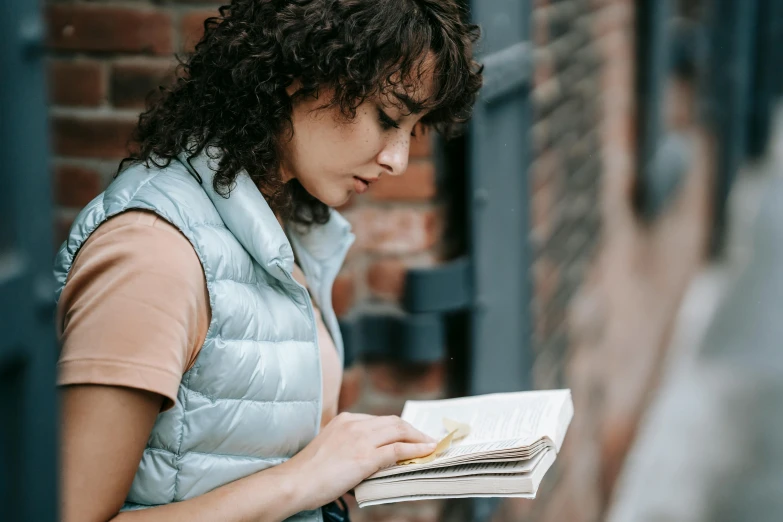 a woman reading a book while standing in front of a brick building