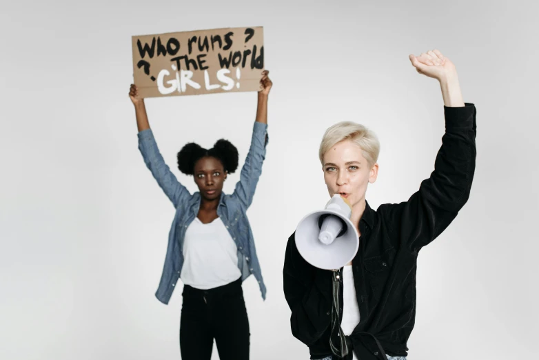 two women holding placards and yelling and one holding sign that says who runs the world girls