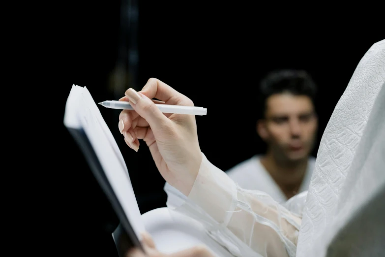 a person wearing white clothes holding a pencil and reading a book