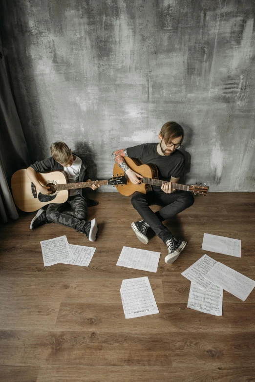 two boys are playing guitar next to an unmade wall