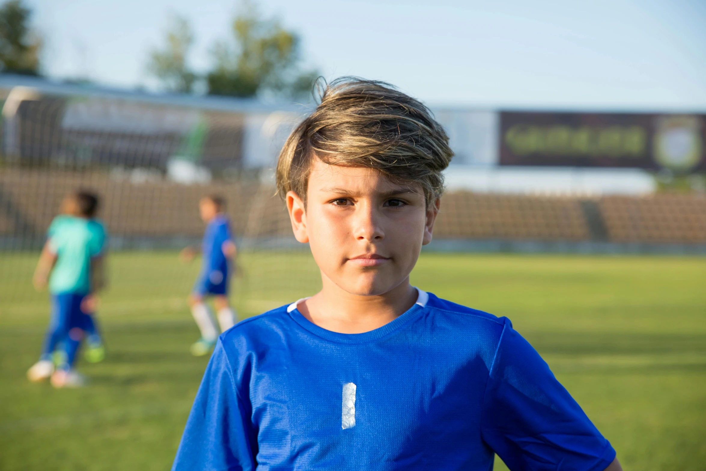 a boy stands before a soccer field wearing a blue uniform