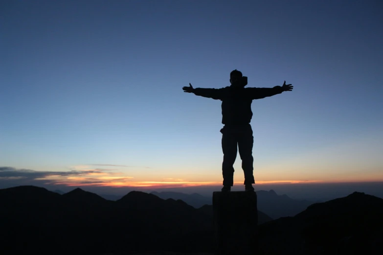 the silhouette of a man standing on a large rock