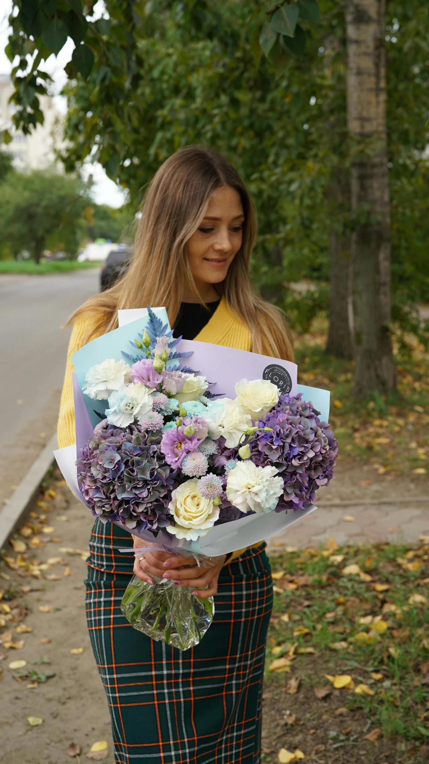 a woman standing on the sidewalk holding a bouquet of flowers