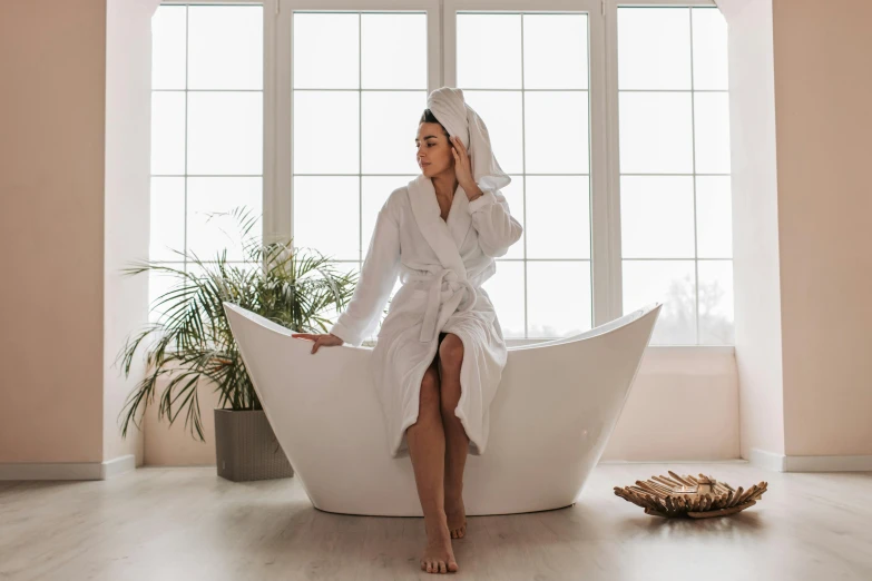a woman wearing a white robe and head covering, sitting in an odd shaped bathtub